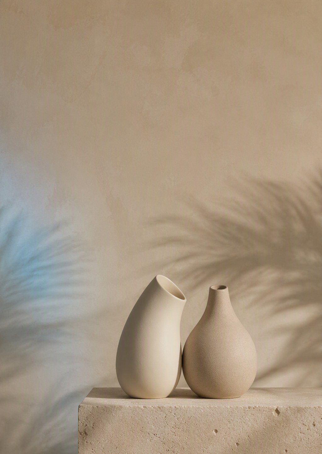 Two ceramic vessels leaning toward each other in quiet conversation on a travertine pedestal — DouVibe confidential contact for the UAE